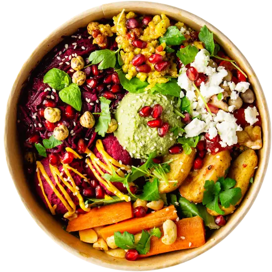 Een kleurrijke saladebowl gevuld met verschillende ingrediënten zoals rode biet, gegrilde wortelen, aardappelen, kikkererwten, hummus, fetakaas, granaatappelpitjes, groene bladeren, en specerijen, geserveerd in een ronde kom