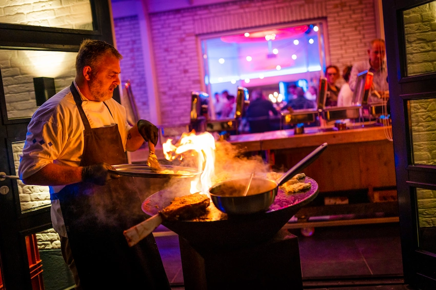 Een kok staat te grillen bij de barbecue, terwijl de vlammen omhoog schieten van de grill.