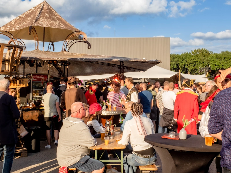 Bezoekers genieten van een piratenfeest, gekleed in piratenkostuums, terwijl ze drinken en praten bij een buitenevenement