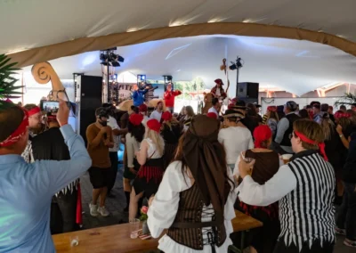 Een piratenfeest in volle gang onder een grote tent, met deelnemers in piratenkostuums die dansen en genieten van de muziek