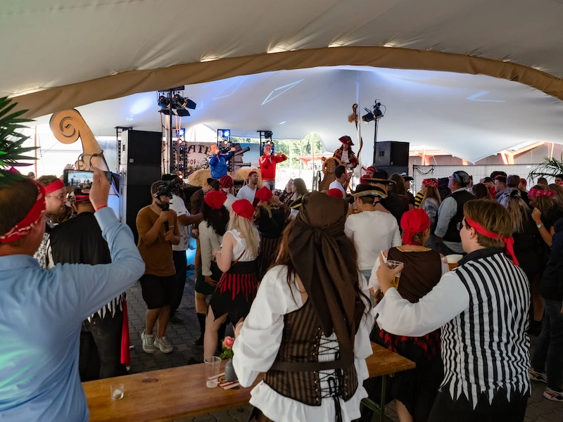 Een piratenfeest in volle gang onder een grote tent, met deelnemers in piratenkostuums die dansen en genieten van de muziek