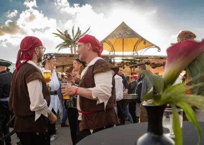 Piratenfeest in volle gang, met mensen verkleed als piraten die genieten van drankjes en gesprekken in een levendige sfeer