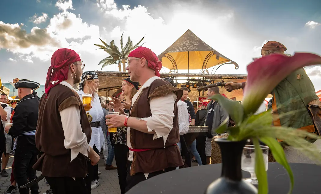 Piratenfeest in volle gang, met mensen verkleed als piraten die genieten van drankjes en gesprekken in een levendige sfeer