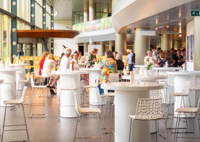 Gasten genieten van een bijeenkomst in een moderne ruimte met grote ramen, ronde tafels en comfortabele stoelen